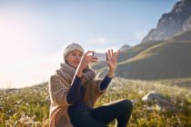 Giovane donna che utilizza il telefono della fotocamera in soleggiata, valle remota — Foto stock