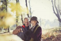 Smiling senior couple using cell phone in sunny autumn park — Stock Photo