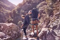 Young couple with backpacks hiking over sunny rocks — Stock Photo