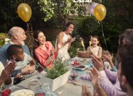 Multi-ethnic multi-generation family clapping celebrating birthday with fireworks cake at patio table — Stock Photo