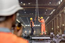 Steel workers adjusting crane hooks in factory — Stock Photo