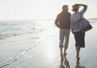 Ältere Paare spazieren am sonnigen Strand des Ozeans — Stockfoto