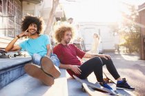 Portrait confident male friends with skateboards hanging out on sunny urban steps — Stock Photo