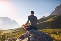 Giovane uomo che medita sulla roccia in una valle soleggiata e remota — Foto stock