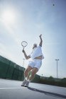 Jeune joueur de tennis masculin jouant au tennis, servant la balle sur un court de tennis ensoleillé — Photo de stock
