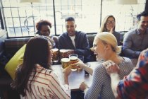 Amici che ridono brindando bicchieri di birra a tavola nel bar — Foto stock