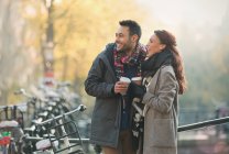 Sonriendo joven pareja en ropa de abrigo beber café en la ciudad - foto de stock