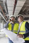Ingénieurs masculins avec lampe de poche et plans directeurs regardant vers le haut sur le chantier — Photo de stock