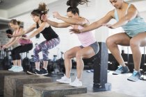 Determined women doing jump squats on boxes in exercise class — Stock Photo