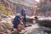 Coppia giovane con zaini trekking, spruzzi d'acqua al torrente — Foto stock