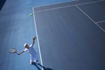 Вид сверху молодой теннисист, играющий в теннис, подающий мяч на солнечно-синем теннисном корте — стоковое фото