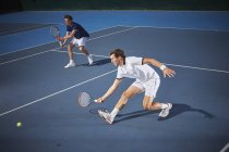 Young male tennis doubles players playing tennis, reaching with tennis racket on blue tennis court — Stock Photo