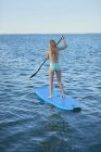 Young woman in bikini paddleboarding in summer ocean — Stock Photo
