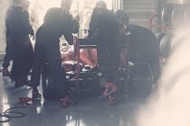 Команда пит-стопа работает над гоночным автомобилем Формулы 1 в ремонтном гараже — стоковое фото