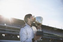 Male formula one driver kissing trophy, celebrating victory on sports track — Stock Photo