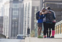 Runners connected in a huddle on sunny urban sidewalk — Stock Photo