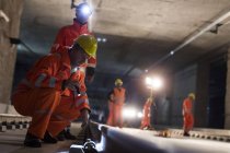 Trabajadores de la construcción examinando vías subterráneas en obra subterránea oscura - foto de stock