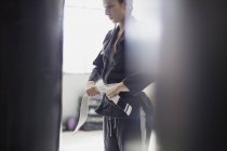 Mujer joven atando cinturón de judo en el gimnasio - foto de stock