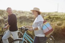 Mature couple walking bicycles on sunny beach grass path — Stock Photo