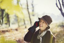 Senior woman talking on cell phone in sunny autumn park — Stock Photo