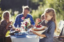 Fille tenant gâteau aux fraises à la table de patio de fête de jardin ensoleillé — Photo de stock