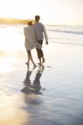 Junges Paar hält Händchen und geht bei Sonnenuntergang am Strand spazieren — Stockfoto