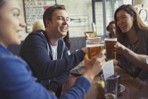 Amici che festeggiano, brindando birra e bicchieri di vino a tavola nel bar — Foto stock