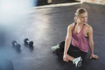 Young woman stretching, twisting in gym next to dumbbells — Stock Photo