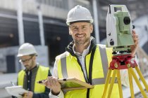 Retrato sonriente ingeniero masculino usando teodolito en el sitio de construcción - foto de stock