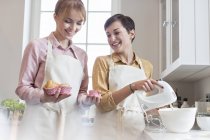 Усміхнені жіночі прибиральники випікають кекси на кухні — стокове фото