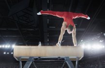 Male gymnast performing upside-down handstand on pommel horse in arena — Stock Photo