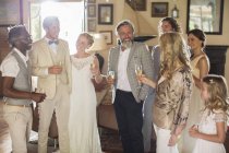 Jeune couple avec invités et flûtes à champagne à la réception de mariage — Photo de stock