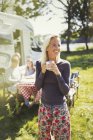 Smiling woman in pajamas drinking coffee outside sunny motor home — Stock Photo
