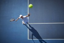 Vista aerea del giovane tennista maschile che gioca a tennis, servendo la palla sul soleggiato campo da tennis blu — Foto stock