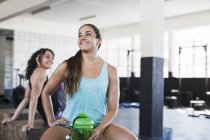 Lächelnde junge Frau ruht sich aus und trinkt Wasser nach dem Training im Fitnessstudio — Stockfoto