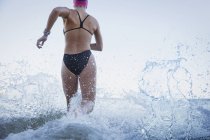 Mujer nadadora de aguas abiertas corriendo y salpicando en el océano surf - foto de stock