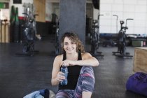 Portrait souriant, confiant jeune femme boire de l'eau et de repos après l'entraînement dans la salle de gym — Photo de stock