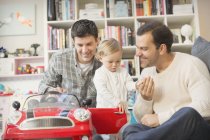 Male gay parents and baby son playing with toy car — Stock Photo