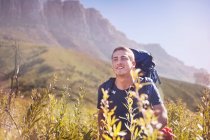 Young man with backpack hiking in sunny valley — Stock Photo