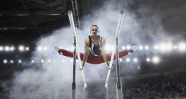 Focado ginasta masculino realizando divisões em barras paralelas na arena — Fotografia de Stock