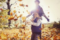 Verspielte Mutter und Tochter werfen Herbstblätter in sonnigem Park — Stockfoto