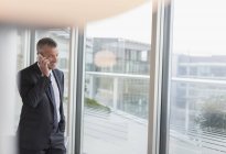 Uomo d'affari che parla al cellulare alla finestra dell'ufficio — Foto stock