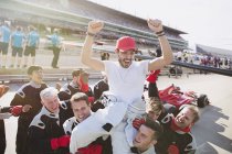 Formula one racing team carrying driver on shoulders, celebrating victory on sports track — Stock Photo