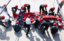 Manager with stopwatch timing pit crew replacing tires on formula one race car in pit lane — Stock Photo