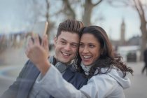 Smiling couple taking selfie with camera phone in urban park — Stock Photo