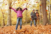 Verspieltes Mädchen wirft Herbstblätter in den Wald — Stockfoto