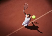 Visão aérea jovem jogador de tênis masculino jogando tênis, servindo a bola no campo de tênis ensolarado — Fotografia de Stock