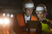 Travailleur de la construction et ingénieur utilisant une tablette numérique sur le chantier sombre — Photo de stock