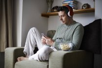 Man sitting in armchair with headphones using smartphone — Stock Photo