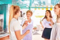 Senior female business owner serving ice cream to young women at food cart — Stock Photo
